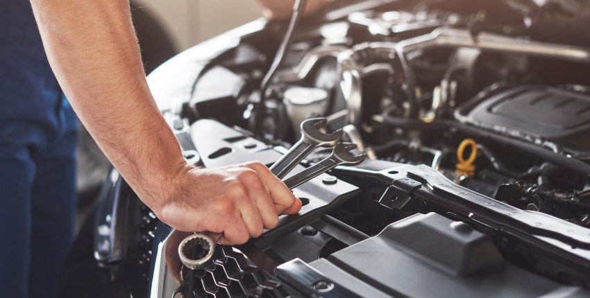 Mechanic standing in front of engine bay with a wrench