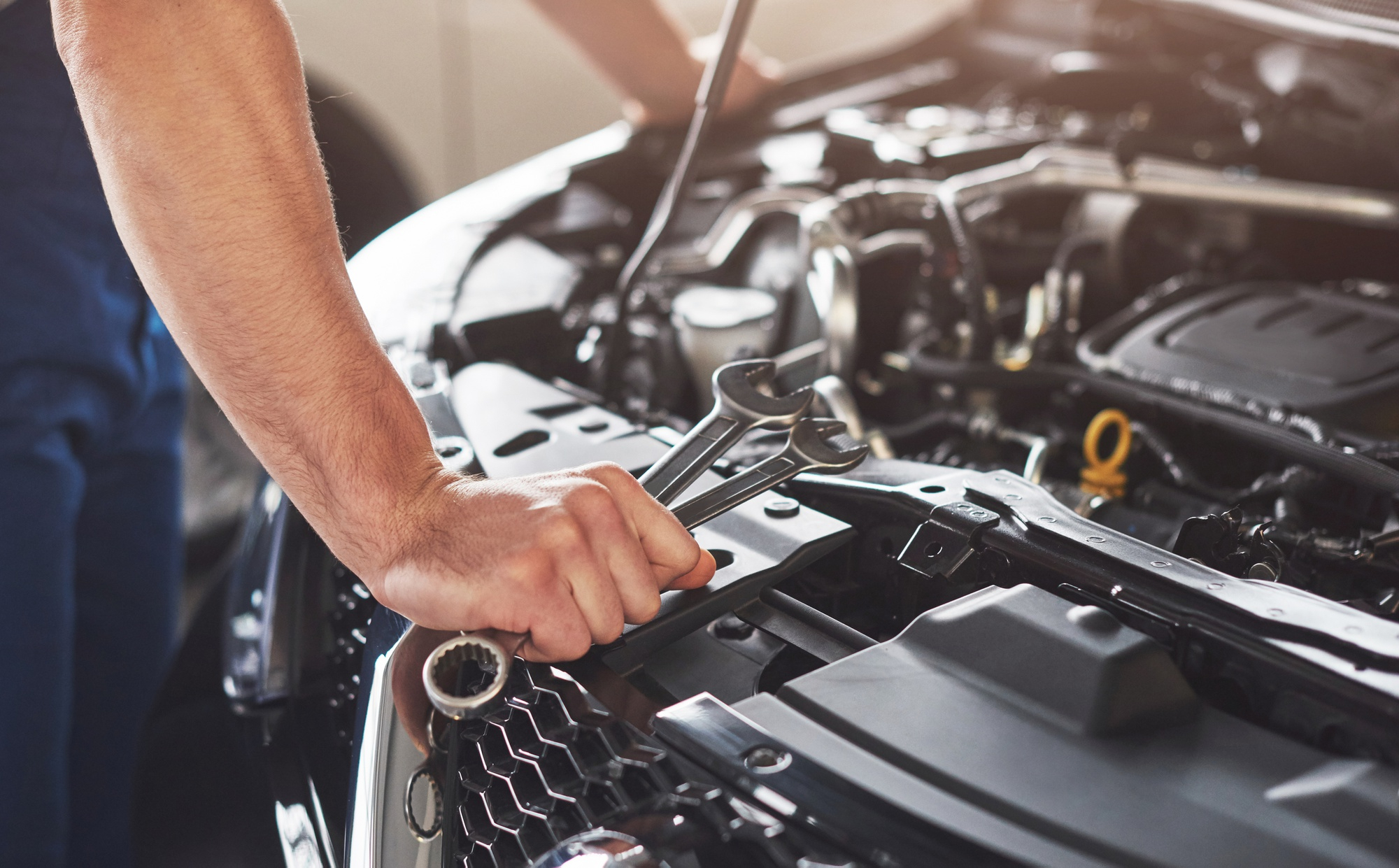 Mechanic standing in front of engine bay with a wrench